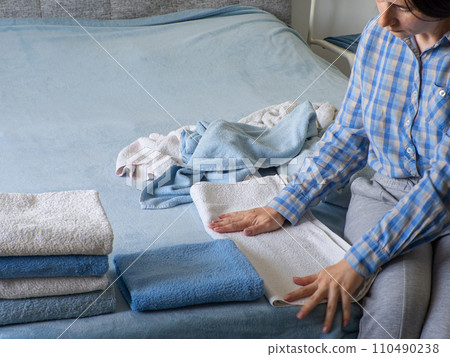 Woman folding clean terry towel in the bedroom. Organizing laundry at home. 110490238
