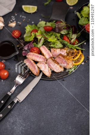 sliced grilled Organic Tuna Steak on black ceramic serving dish with salad on a table 110491297