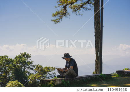 landscape and travel concept with solo freelancer man sit on wooden and use tablet work from outdoor with layer of mountain background landscape and travel concept with solo freelancer man sit on wooden and use tablet work from outdoor with layer of mountain background 110491638