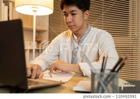 Working in the middle of the night, Man sat typing away on a laptop in his office with a determined look on his face, Male hand pressing on laptop keyboard. Working in the middle of the night, Man sat typing away on a laptop in his office with a determined look on his face, Male hand pressing on laptop keyboard. 110492091