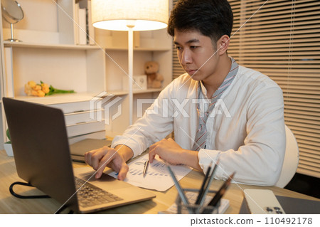 Working in the middle of the night, Man sat typing away on a laptop in his office with a determined look on his face, Male hand pressing on laptop keyboard. Working in the middle of the night, Man sat typing away on a laptop in his office with a determined look on his face, Male hand pressing on laptop keyboard. 110492178