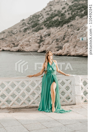 Woman sea green dress. Side view a happy woman with long hair in a long mint dress posing on a beach with calm sea bokeh lights on sunny day. Girl on the nature on blue sky background. 110492841