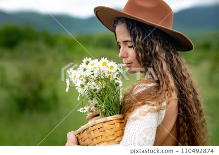 A middle-aged woman in a white dress and brown hat holds a lA middle-aged woman in a white dress and brown hat holds a basket in her hands with a large bouquet of daisies.arge bouquet of daisies in A middle-aged woman in a white dress and brown hat holds a lA middle-aged woman in a white dress and brown hat holds a basket in her hands with a large bouquet of daisies.arge bouquet of daisies in 110492874