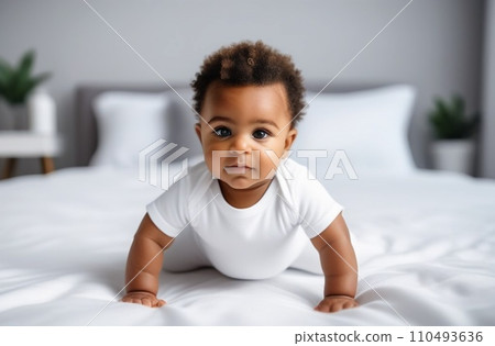Portrait of cute little African baby wearing bodysuit lying on white beedsheets at home. Selective focus, 110493636