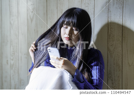 A young woman using a smartphone in a room where she lives alone A young woman using a smartphone in a room where she lives alone 110494547