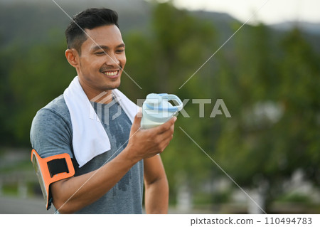 Active sportsman holding protein supplement shaker taking a break at outdoor 110494783