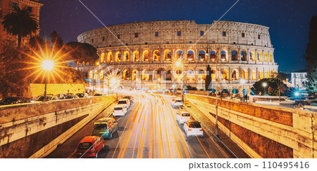 Rome, Italy. Colosseum Also Known As Flavian Amphitheatre In Evening Or Night Time. Night Traffic Light Trails Near Famous World Landmark. Amazing Night Starry Sky Background. Bright Blue Night Sky 110495416
