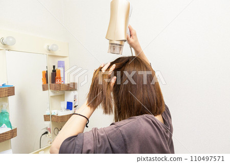 Woman drying her hair with a hair dryer in the bathroom Woman drying her hair with a hair dryer in the bathroom 110497571
