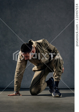 Unusual male with tattooed body and face, earrings, beard. Dressed in khaki jumpsuit, black sneakers. Dancing on gray background. Dancehall, hip-hop Unusual male with tattooed body and face, earrings, beard. Dressed in khaki jumpsuit, black sneakers. Dancing on gray background. Dancehall, hip-hop 110497654