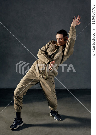Stately guy with tattooed body and face, earrings, beard. Dressed in khaki overalls and black sneakers. Dancing on gray background. Dancehall, hip-hop Stately guy with tattooed body and face, earrings, beard. Dressed in khaki overalls and black sneakers. Dancing on gray background. Dancehall, hip-hop 110497703