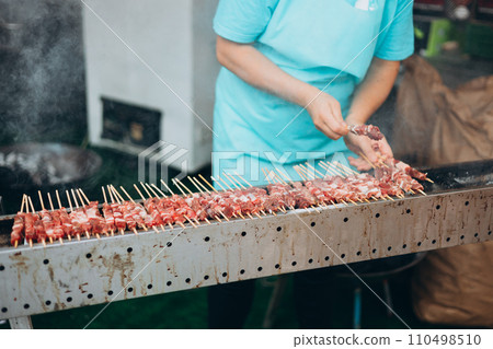 Focus selection: Pork grilled vendors, street food available in Thailand. Hand of a hawker grilled pork and beef over an open fire. Selling traditional hot food at the Fair 110498510