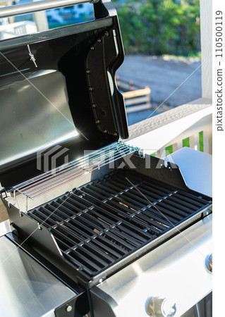 Close-up reveals the pristine griddle of a new two-burner grill, prominently displayed on the balcony of a suburban house, eagerly awaiting its first outdoor cooking adventure. Close-up reveals the pristine griddle of a new two-burner grill, prominently displayed on the balcony of a suburban house, eagerly awaiting its first outdoor cooking adventure. 110500119