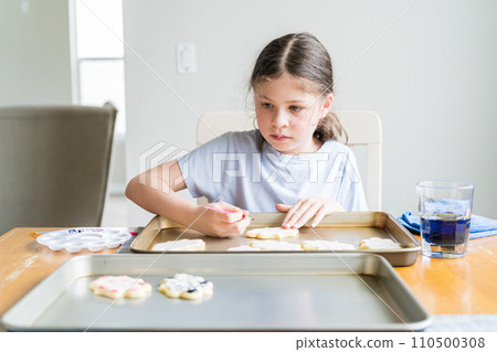 A heartwarming scene of a little girl carefully writing 'Sorry' on sugar cookies with food coloring, the cookies beautifully flooded with white royal icing. A heartwarming scene of a little girl carefully writing 'Sorry' on sugar cookies with food coloring, the cookies beautifully flooded with white royal icing. 110500308
