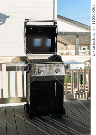 Sleek, open-lid, two-burner grill stands ready for use, conveniently positioned on the balcony of a suburban home, promising a delightful alfresco cooking experience. 110500365