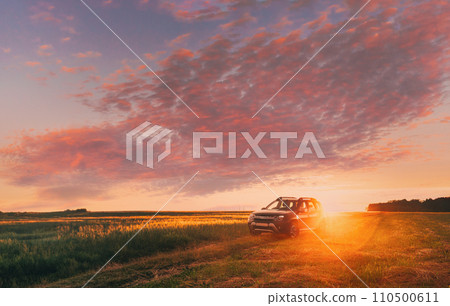 AWD 4WD SUV green car in summer meadow landscape in summer field countryside landscape. Sunset sky background 110500611