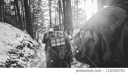 Group Of Soldiers Sub-machine Guns And Bazooka Marching In Forest. Re-enactors Dressed As German Infantry Soldier Marching Through Forest Road In Winter Day. Wehrmacht Army Soldiers Of World War Ii 110500761