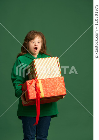 Emotional teen girl with down syndrome standing with socked face, holding many present boxes against green studio background 110501975