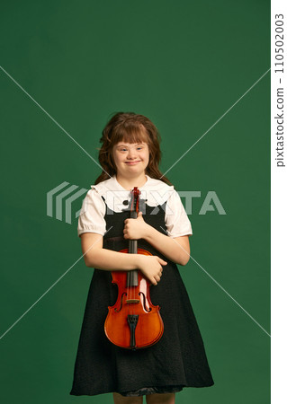Beautiful girl with down syndrome standing with violin, learning music against green studio background Beautiful girl with down syndrome standing with violin, learning music against green studio background 110502003