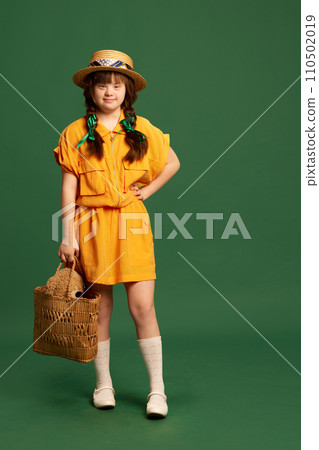Beautiful teen girl with down syndrome wearing yellow dress and hat standing against green studio background Beautiful teen girl with down syndrome wearing yellow dress and hat standing against green studio background 110502019