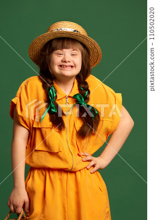 Beautiful smiling teen girl with down syndrome wearing yellow dress and hat standing against green studio background Beautiful smiling teen girl with down syndrome wearing yellow dress and hat standing against green studio background 110502020