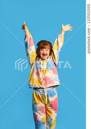 Smiling girl with dawn syndrome expressing happiness and joy against blue studio background. Tolerance, support and care 110502058