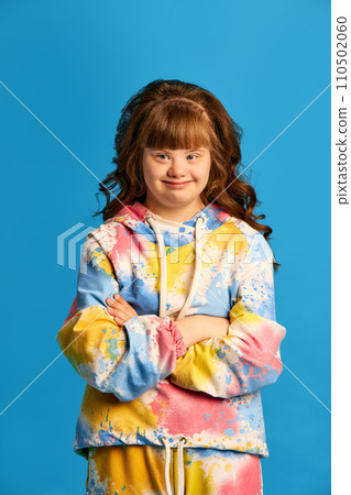 Portrait of young beautiful teen girl with down syndrome, wearing colorful clothes, smiling against blue studio background Portrait of young beautiful teen girl with down syndrome, wearing colorful clothes, smiling against blue studio background 110502060