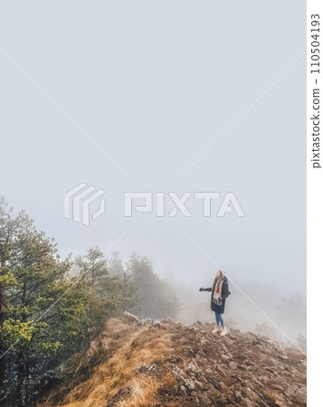 Woman Standing on Rock Looking at Forest in Fog 110504193