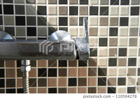 Limescale on the dirty faucet switch in the shower room. Brown tiles on the wall. 110504278