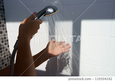 Female hand touching water pouring from a rain shower head, checking water temperature. 110504282