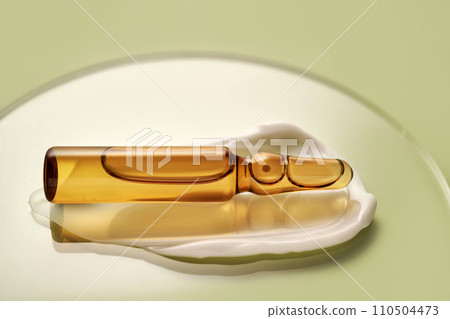 Ampoule in a drop of cosmetic cream on a green background. 110504473