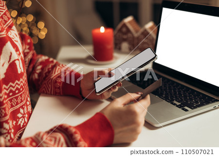 woman holding credit card and using smart phone at home office during christmas holidays on a laptop background woman holding credit card and using smart phone at home office during christmas holidays on a laptop background 110507021