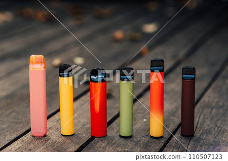 Vaping devices. Set of colorful electronic cigarettes. Electronic sticks for vaping on wood background Vaping devices. Set of colorful electronic cigarettes. Electronic sticks for vaping on wood background 110507123