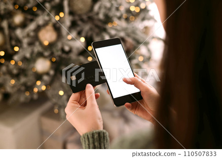 Christmas online shopping, Female hands holds the phone with credit card and blurred bokeh lights 110507833