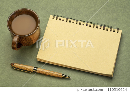 blank spiral sketchbook against textured paper with a cup of coffee, desktop flat lay 110510624