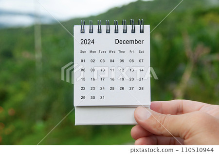 Hand holding December 2024 white calendar with nature background. Holiday and calendar concept 110510944