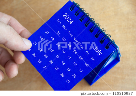 Hand showing July 2024 table calendar on wooden background. Calendar and new month concept. Hand showing July 2024 table calendar on wooden background. Calendar and new month concept. 110510987