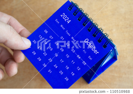 Hand showing October 2024 table calendar on wooden background. Calendar and new month concept. Hand showing October 2024 table calendar on wooden background. Calendar and new month concept. 110510988