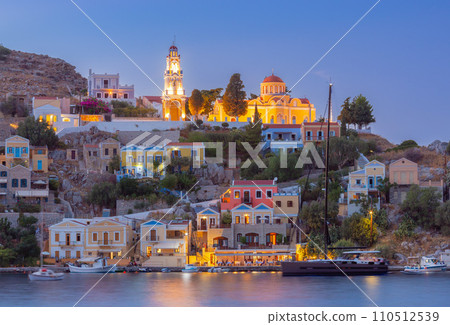 Multi-colored facades of houses in the light of lanterns in the village of Symi at sunset. 110512539