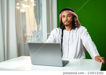 Young Arab man in traditional dress thobe working on computer in office 110513292
