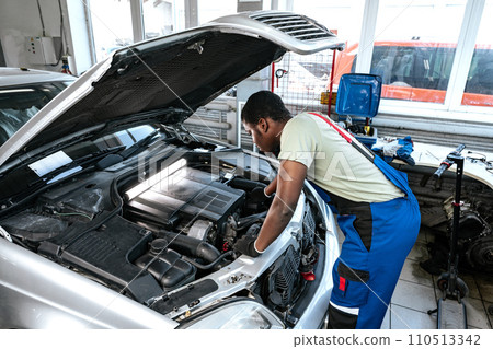Young African man working under the hood of car fixing engine in auto service 110513342