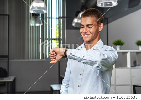 Young businessman looking at his watch checking the time in the office Young businessman looking at his watch checking the time in the office 110513535