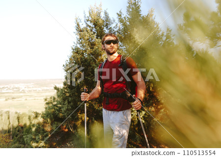 Young man hiker travels through the mountains with trekking poles for nordic walking Young man hiker travels through the mountains with trekking poles for nordic walking 110513554