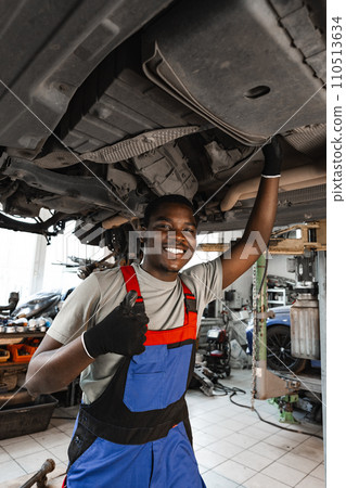 Young African mechanic in uniform working under the car in car service center Young African mechanic in uniform working under the car in car service center 110513634
