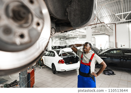 Pensive young African mechanic in car service looking at car thinking of how to repair it 110513644