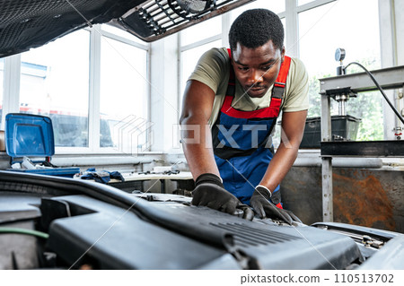 Young African man working under the hood of car fixing engine in auto service Young African man working under the hood of car fixing engine in auto service 110513702