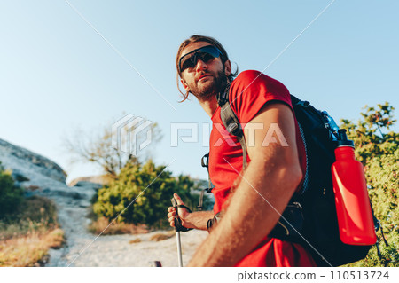 Young man hiker travels through the mountains with trekking poles for nordic walking Young man hiker travels through the mountains with trekking poles for nordic walking 110513724