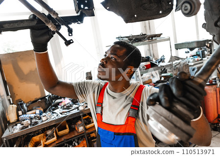 Young African mechanic in uniform working under the car in car service center Young African mechanic in uniform working under the car in car service center 110513971