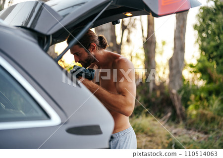 Young man changing clothes on the car trunk after hiking in the woods Young man changing clothes on the car trunk after hiking in the woods 110514063