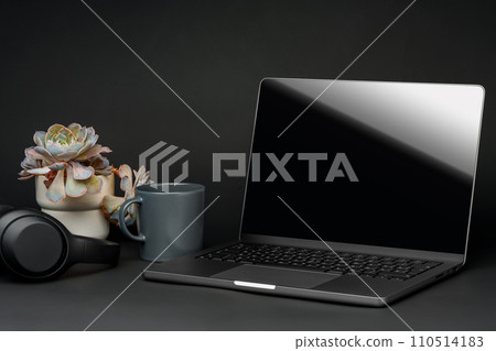 Laptop with black screen on working desk with cup and earphones on black background Laptop with black screen on working desk with cup and earphones on black background 110514183
