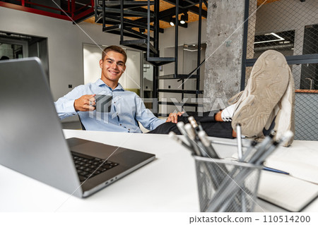 Smiling young businessman relaxing on chair with his feet resting on table 110514200